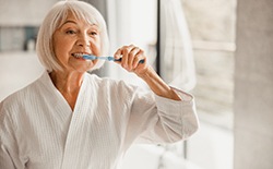 An older woman in a bathrobe brushing her teeth in the morning